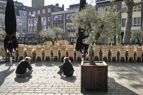 Two young people sit on the ground in the city centre, in a place normally full of pavement cafés.