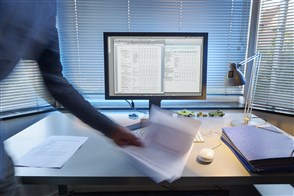 Bureau met pc waarop iemand een stapel papier neerlegt