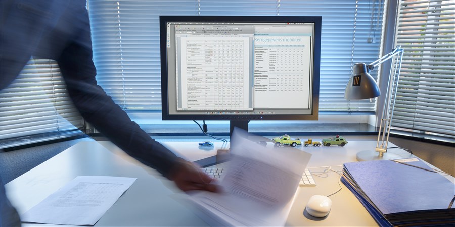 Bureau met pc waarop iemand een stapel papier neerlegt