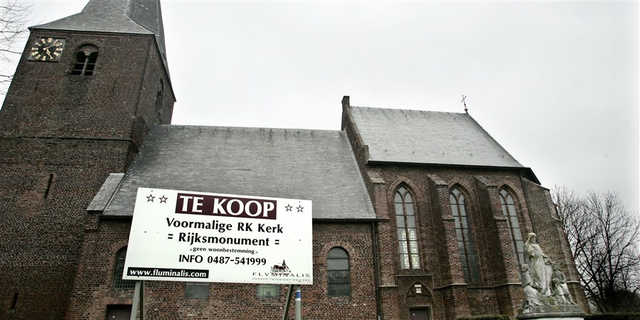 Kerkgebouw te koop. Bord met te koop in de tuin bij de kerk