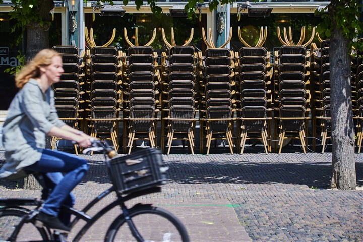 Een vrouw fietst langs opgestapelde terrasstoelen