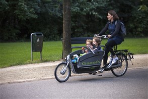 A young mother cycles through the park with her two children on a transport bike.