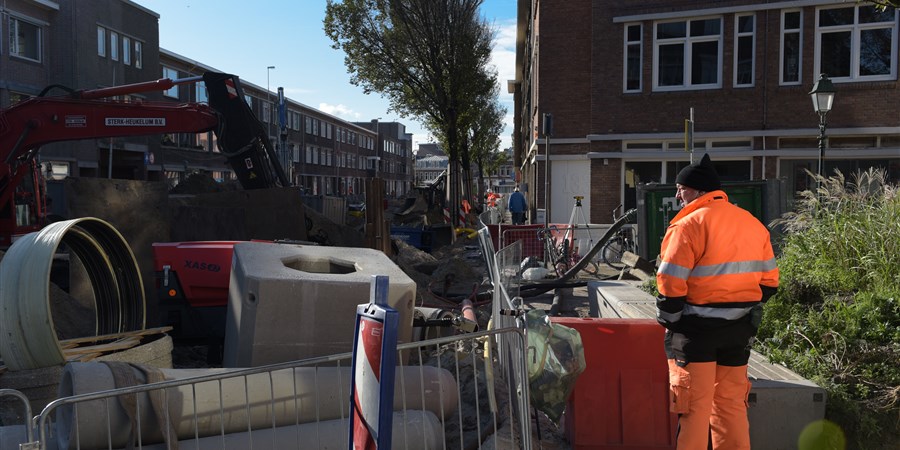 Persoon in werkpak bij werkzaamheden aan riolering in straat