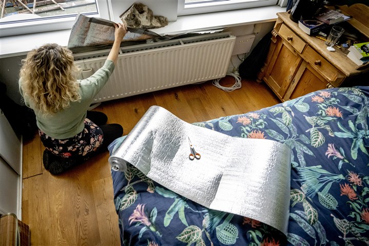 Bewoner bevestigt folie achter radiator om haar woning iets beter te isoleren.
