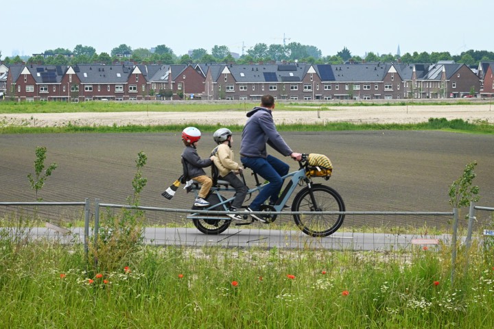 Vader fiets langs nieuwbouwhuizen met kinderen achterop