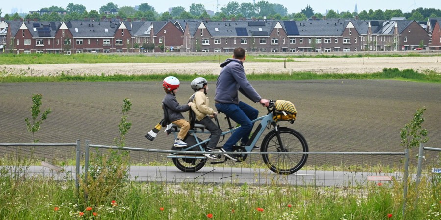 Vader fiets langs nieuwbouwhuizen met kinderen achterop