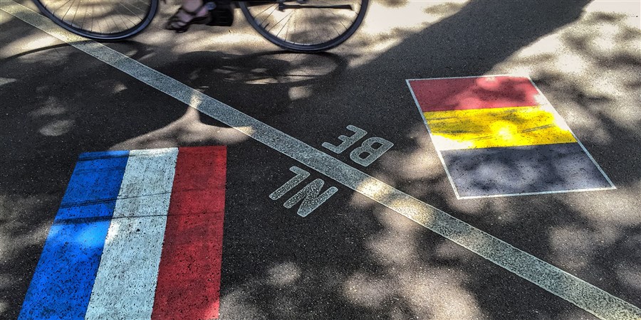 Mevrouw op de fiets die de grens tussen België en Nederland oversteekt.