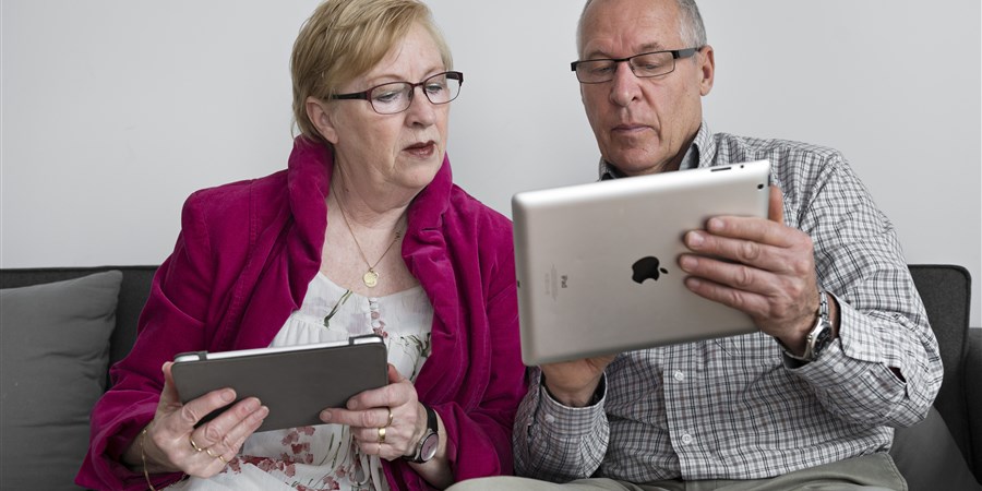 Ouderen die met ipad op de bank zitten en met elkaar meekijken