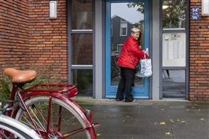 Een vrouw gaat met een volle boodschappentas door de voordeur van haar flat.