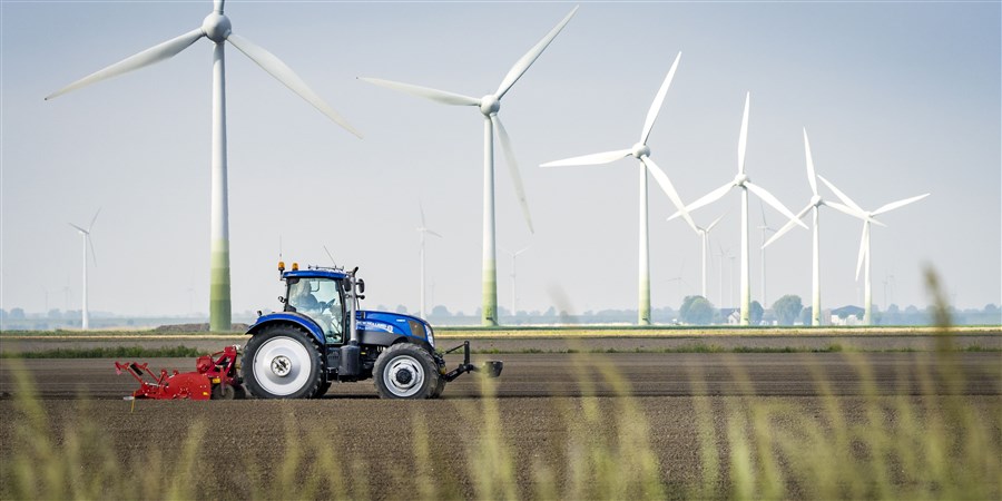 Tractor on farmland and wind turbines in the background