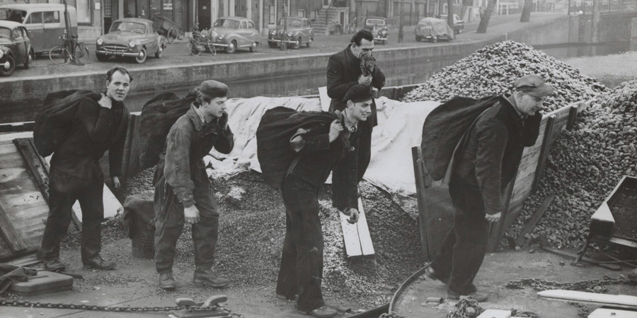 Kolenwerkers vullen zakken met kolen op een kolenschuit. Amsterdam, 1955. Kolenwerkers vullen zakken met kolen op een kolenschuit. Amsterdam, 1955.