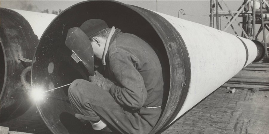 Een lasser aan het werk in een enorme gasbuis, die onderdeel vormt van een gaszinker die Amsterdam-Zuid van gas moet voorzien.