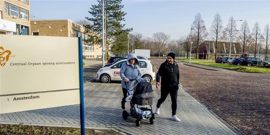 Two asylum seekers walking down the street with a baby stroller.