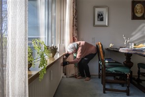 Elderly lady looks at a heater&#x27;s thermostat