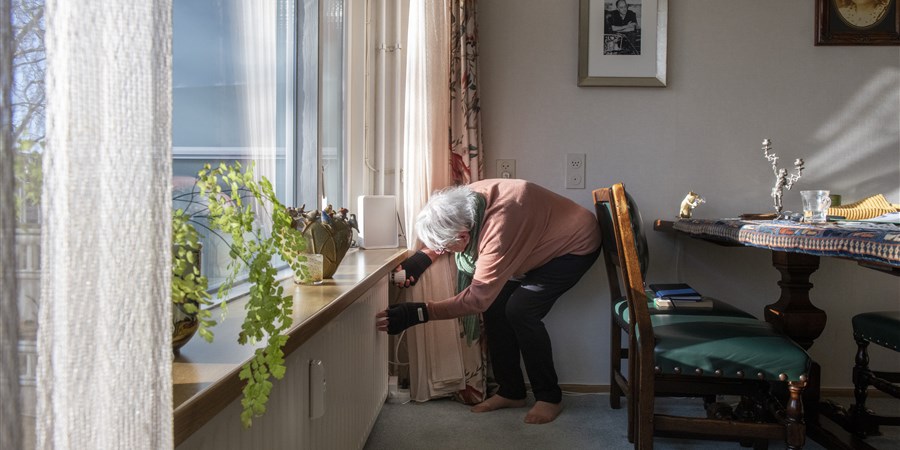 Elderly lady looks at a heater's thermostat