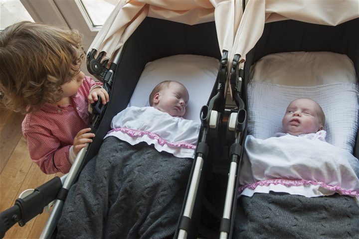 Kleine babietjes thuis, tweeling in een kinderwagen. Grote broer kijkt naar zijn zusjes.