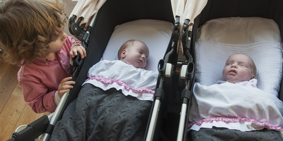 Kleine babietjes thuis, tweeling in een kinderwagen. Grote broer kijkt naar zijn zusjes.