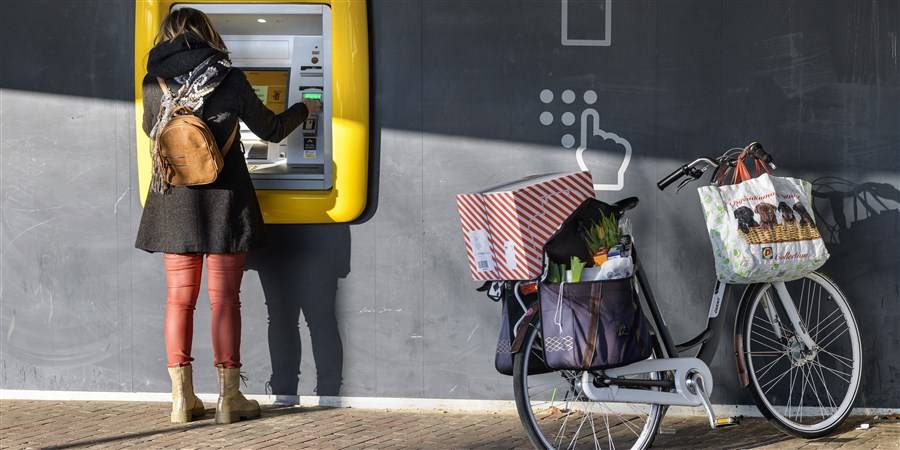 Vrouw met boodschappen bij geldautomaat