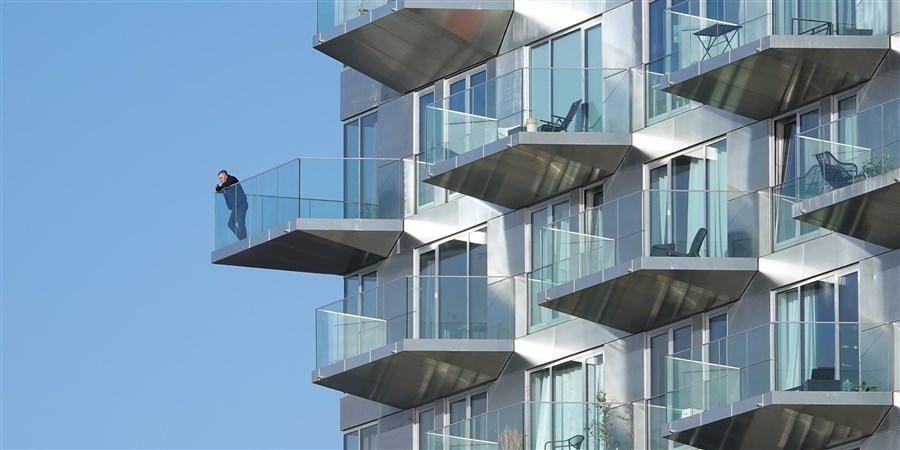 Bewoner kijkt vanaf balkon appartementengebouw..