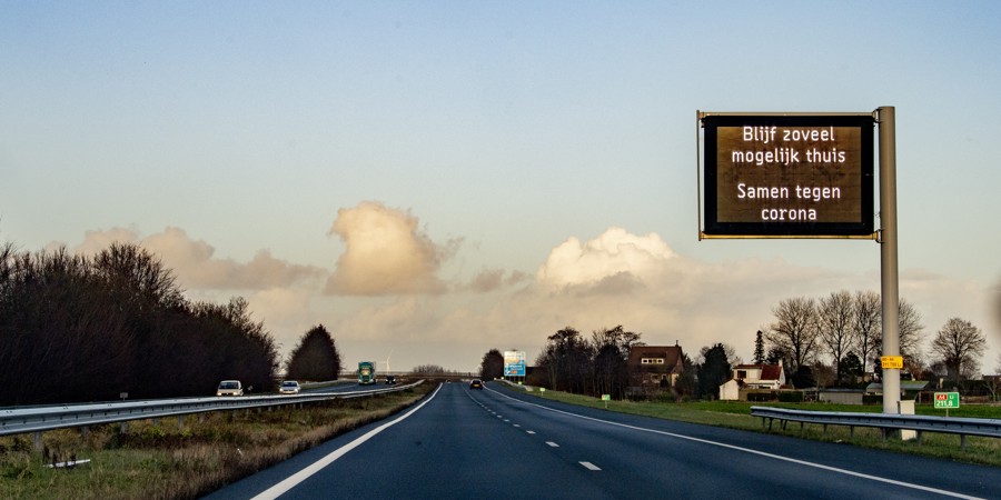 Bord boven lege snelweg met de tekst: Blijf zoveel mogelijk thuis. Samen tegen corona.
