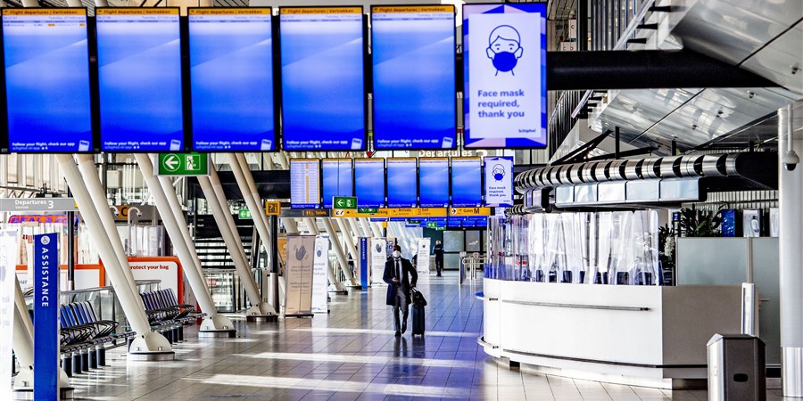 Erg weinig passagiers op Schiphol. Een man met rolkoffer alleen in vertrekhal, coronacrisis.