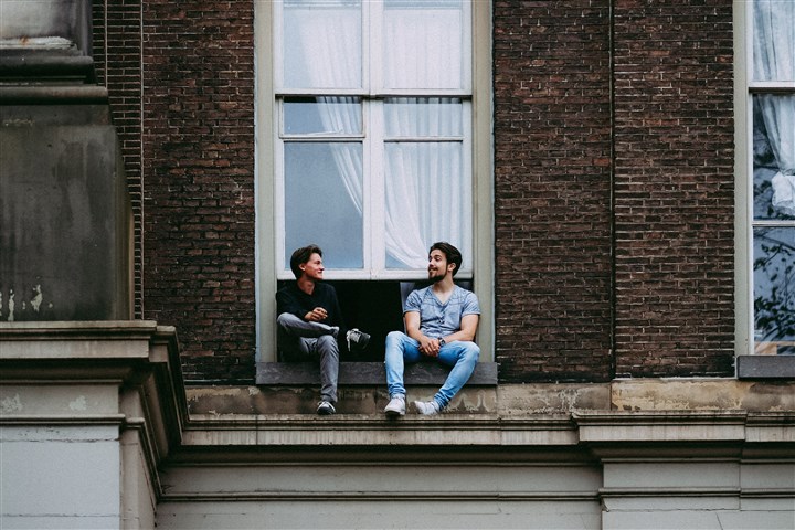 Twee studenten zitten in een raamopening van een studentenhuis.