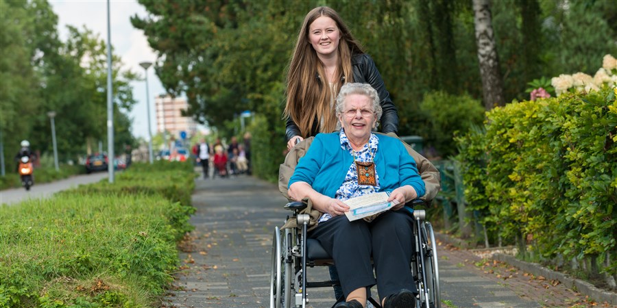 Oudere dame wordt door een meisje in een rolstoel voort geduwd