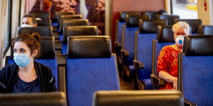 Treinreizigers met mondkapje op afstand van elkaar zittend.