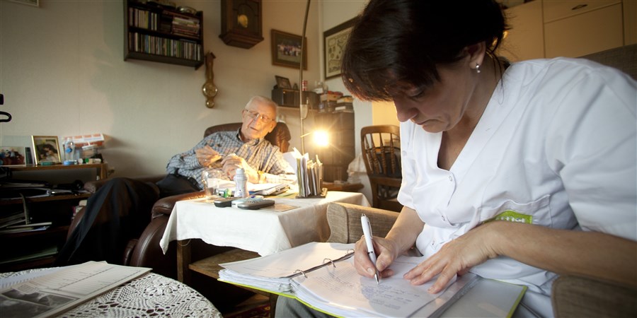 Wijkverpleegkundige op bezoek bij patiënt thuis vult papieren in