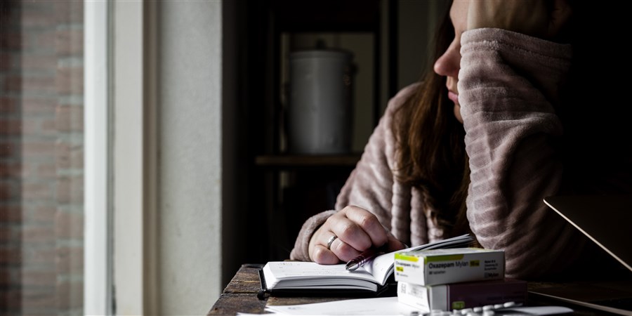 Een vrouw in ochtendjas met gesloten laptop, brieven van het UWV en antidepressiva medicijnen.