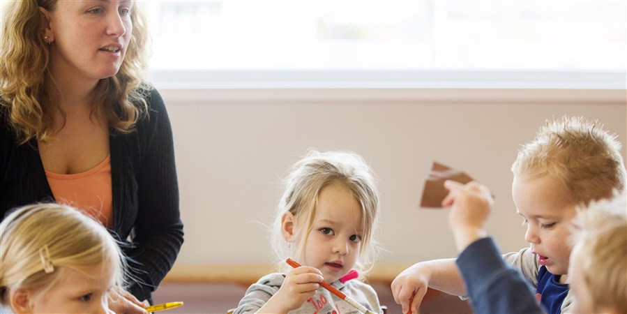 Children cutting and pasting, supervised by a childcare worker.