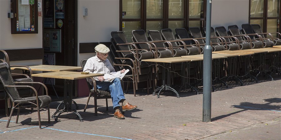 Oudere man zit de krant te lezen op een leeg terras