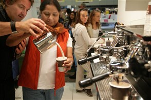 Een horecamedewerker in een kantine leert een nieuwe werkneemster hoe je koffie moet maken
