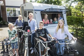 Gezin met acht kinderen poseren met fietsen voor een caravan.