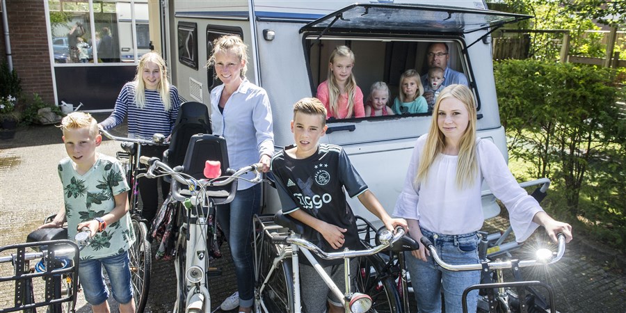 Gezin met acht kinderen poseren met fietsen voor een caravan.