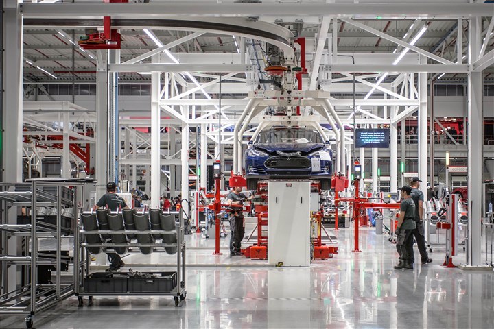 Autofabriek van Tesla in Tilburg waar mensen werken aan auto's die aan de band hangen