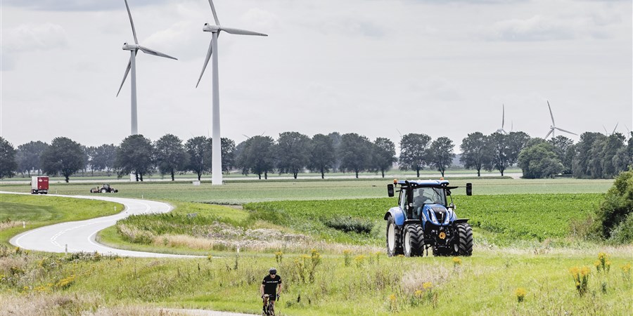 Landschap in Flevoland met windmolens, fietser, vrachtwagen, tractor en boer die mest uitrijdt.