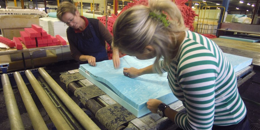 Arbeidskrachten verwerken schuimrubber tot een matras in een schuimrubberfabriek.
