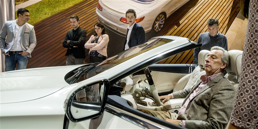 Bezoeker van een lifestylebeurs test de zit van een luxe model cabriolet (uit de 500-serie)