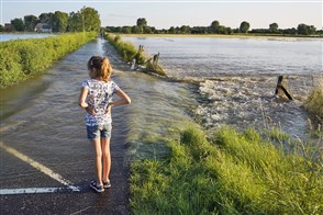 Meisje staat in het water dat over de weg Limburgse uiterwaarden instroomt