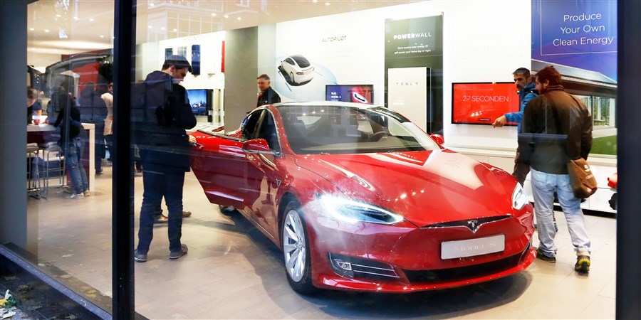 Geïnteresseerden bekijken rode Tesla in winkel