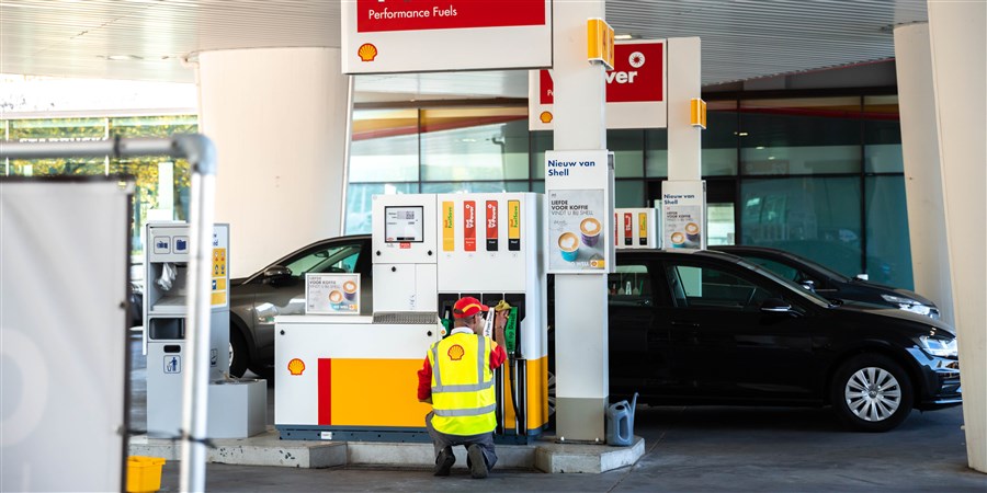 Een man die gehurkt bezig is met het schoonmaken van de benzinepompen in een tankstation