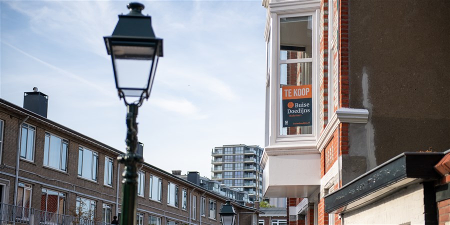 Straatgezicht met flat in de verte, er staat een huis te koop