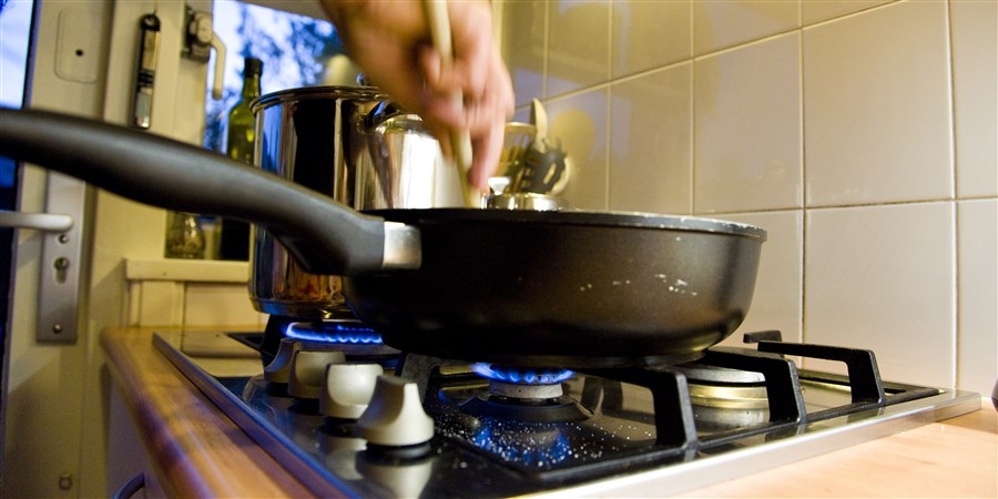 Woman stirs in frying pan on a gas cooker