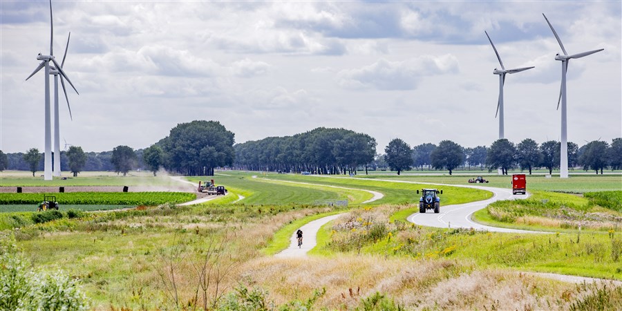 Landschap in Flevoland met windmolens, fietser, vrachtwagen, tractor en boer die mest uitrijdt.