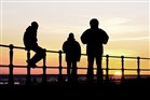 Silhouet van drie jongens op een boulevard aan zee bij zonsondergang