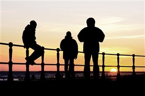 Silhouet van drie jongens op een boulevard aan zee bij zonsondergang