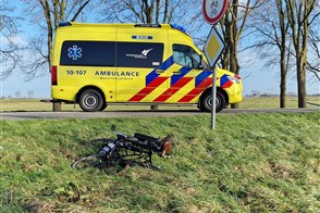 An ambulance drives away, a damaged bike lies in the grass.