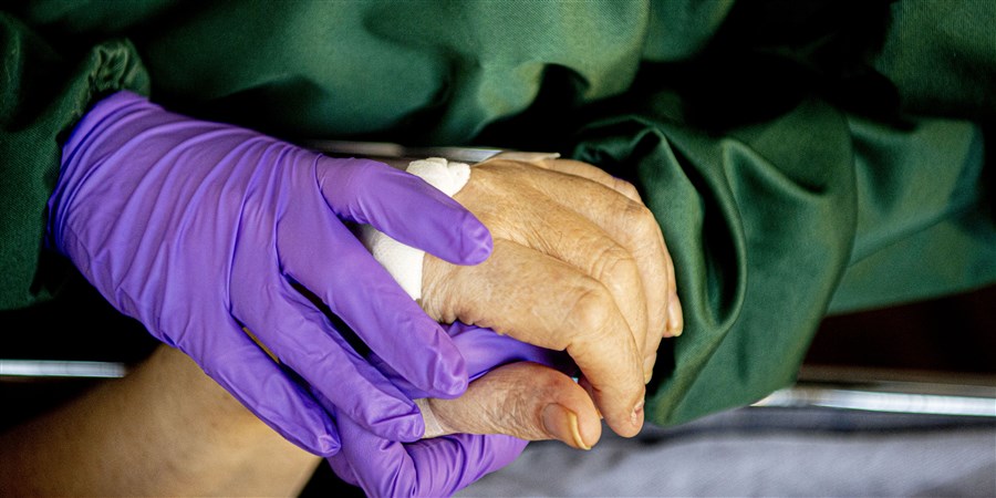 A nurse wearing purple gloves holds the hand of a patient.