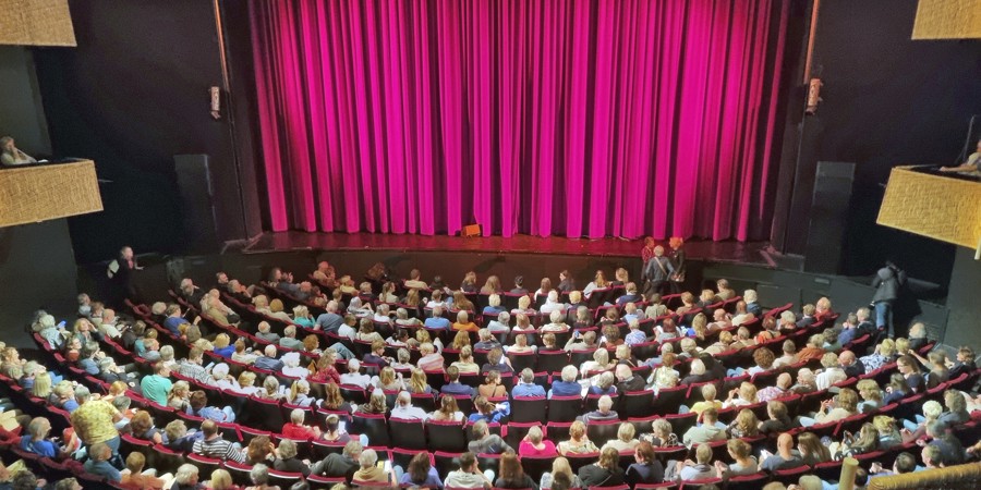 Volle zaal met gesloten gordijn in stadsschouwburg
